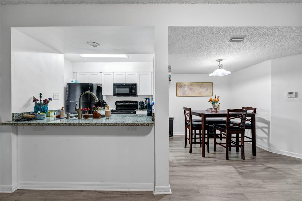 A kitchen with granite countertops and white cabinets opens into a dining area with wood furniture — 202 RIVERBEND DRIVE UNIT 103, ALTAMONTE SPRINGS, FL