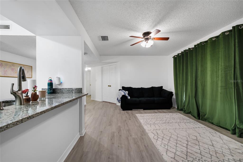 A living room with light wood-look flooring, a black sofa, and green floor-to-ceiling curtains — 202 RIVERBEND DRIVE UNIT 103, ALTAMONTE SPRINGS, FL