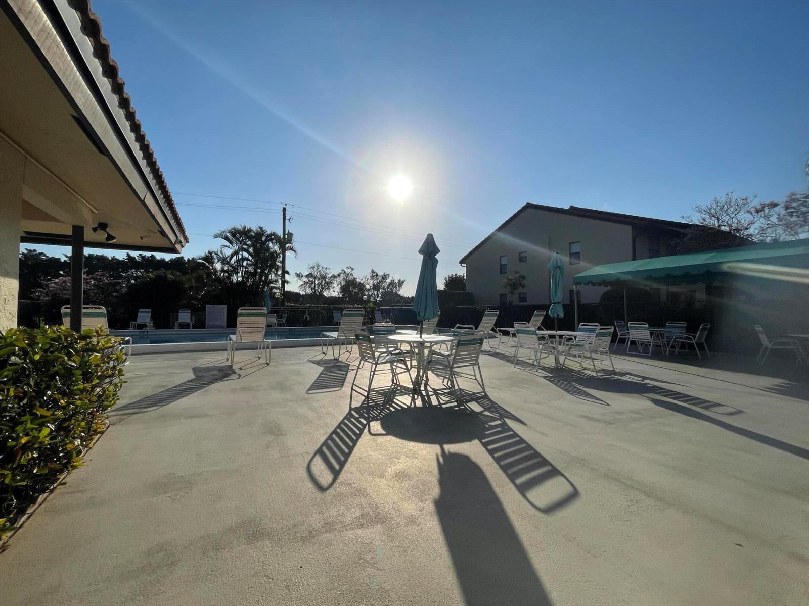 A sunny outdoor pool deck features patio furniture, umbrellas, and a covered seating area — 4682 E Lucerne Lakes Blvd Boulevard E # 202, Lake Worth FL 33467, LAKE WORTH, FL