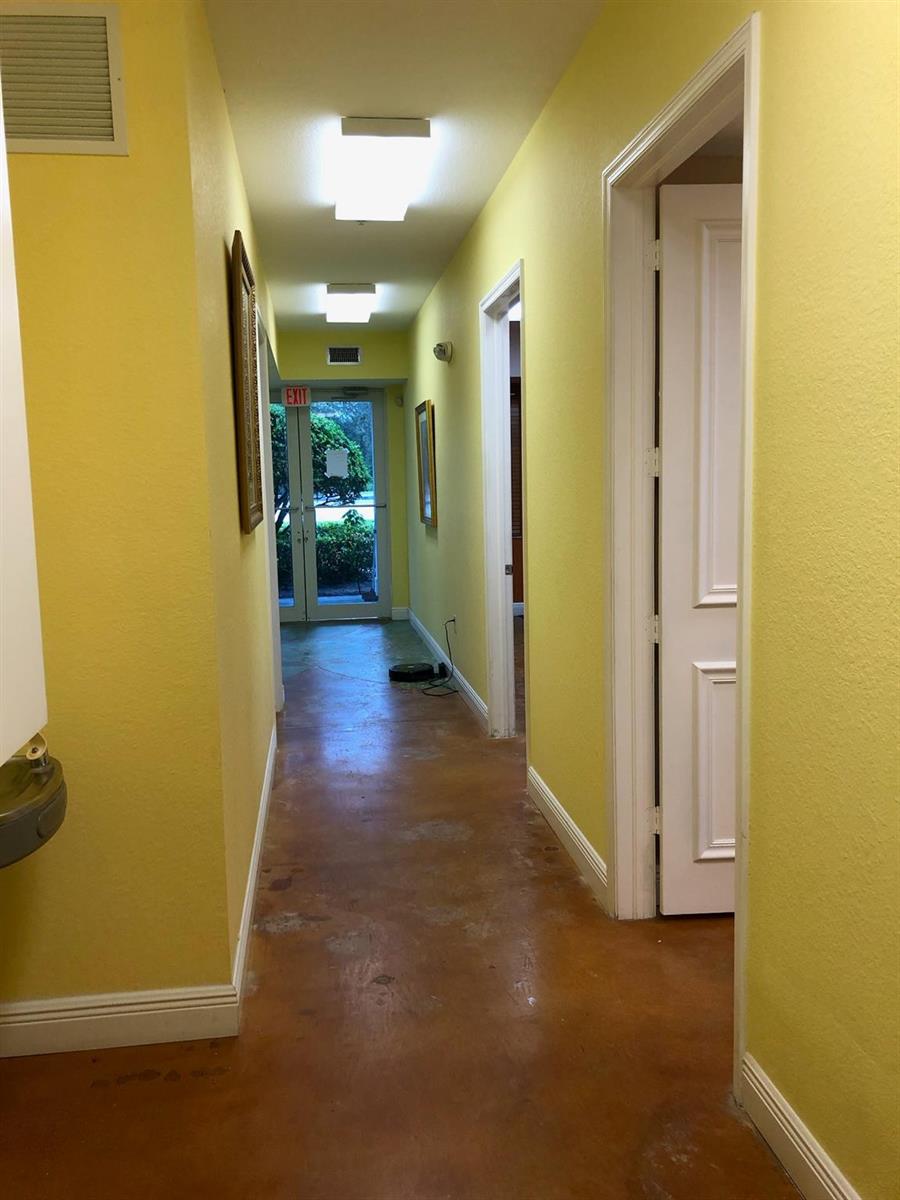 A hallway with yellow walls, a stained concrete floor, and an exit door at the end — 6848 Griffin Road # 6, Davie FL 33314, DAVIE, FL