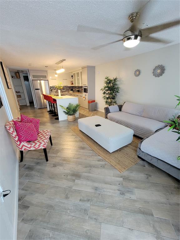 An open-concept living room and kitchen featuring light wood-look flooring and a gray sectional sofa — 7 TRINTARIAS ST., JARDINES DE DORADO DEV. UNIT C-12, DORADO, PR