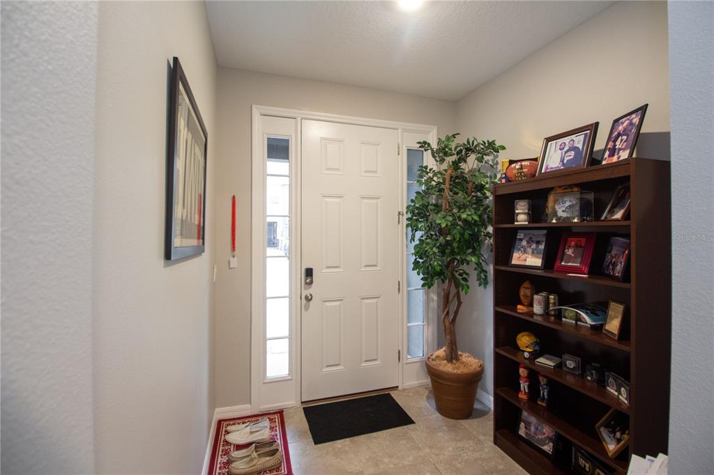 An entryway features a white front door, a tall potted plant, and a wooden bookshelf — 2801 MIDNIGHT PEARL DRIVE, SARASOTA, FL