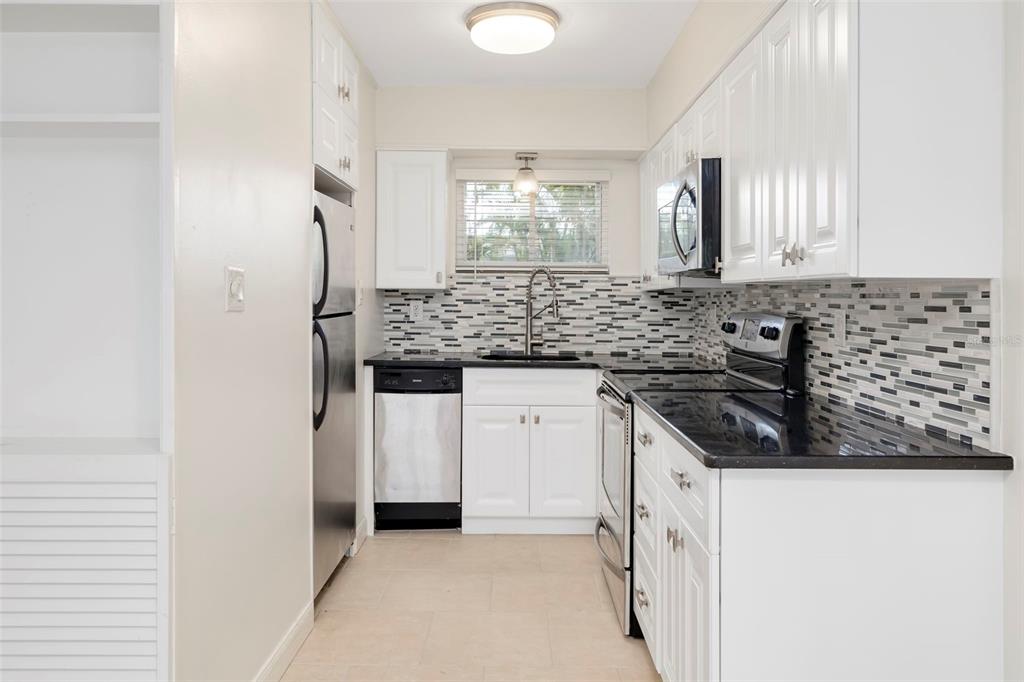 A kitchen with white cabinets, black countertops, stainless steel appliances, and a mosaic tile backsplash — 2155 WOOD STREET UNIT A14, SARASOTA, FL