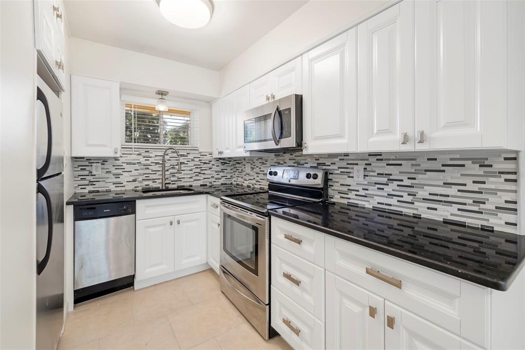 A kitchen features white cabinets, black countertops, stainless steel appliances, and a mosaic tile backsplash — 2155 WOOD STREET UNIT A14, SARASOTA, FL