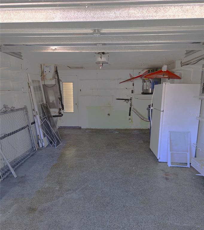 A garage with a concrete floor, a white refrigerator, and various items stored against the walls — 7212 GULF HIGHLANDS DRIVE, PORT RICHEY, FL