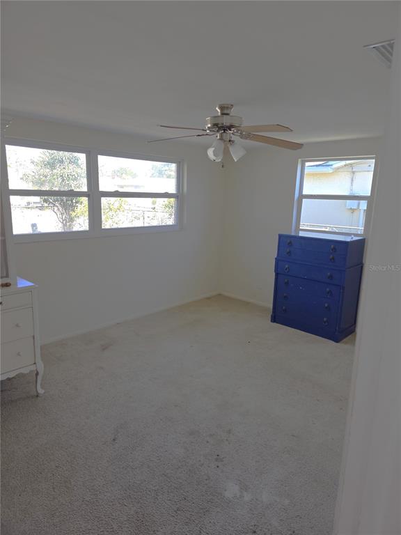 A bedroom with white walls, beige carpeting, a ceiling fan, and two pieces of furniture — 7212 GULF HIGHLANDS DRIVE, PORT RICHEY, FL