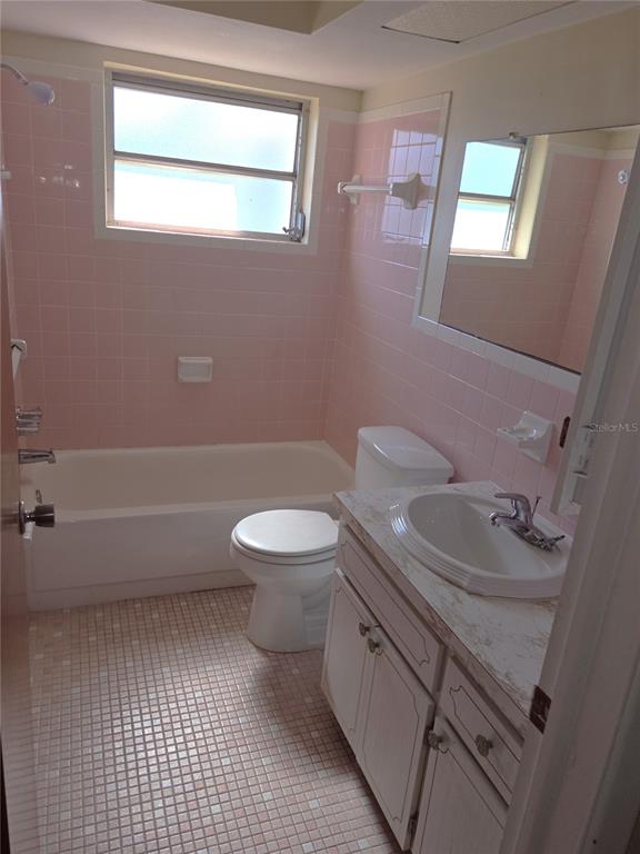 A bathroom features pink wall tiles, a white bathtub, a toilet, and a vanity sink — 7212 GULF HIGHLANDS DRIVE, PORT RICHEY, FL