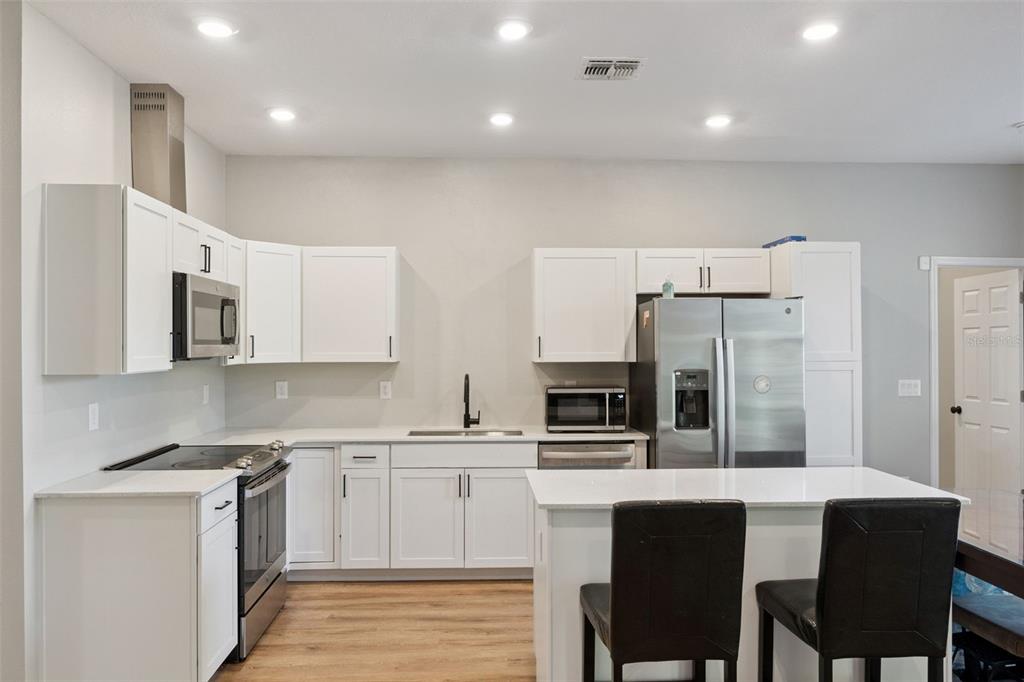 A kitchen features white cabinets, stainless steel appliances, a center island, and light wood flooring — 1403 W KALEY AVENUE, ORLANDO, FL