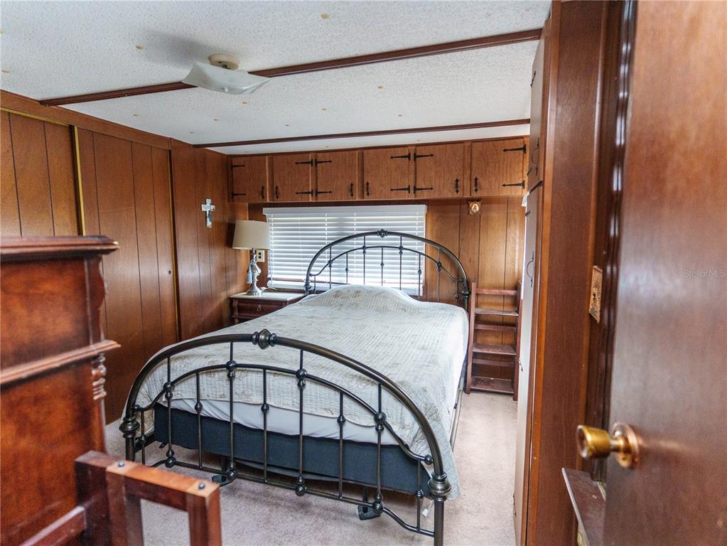 A bedroom features wood-paneled walls, a metal bed frame, and overhead storage cabinets — 5539 OAK RIDGE AVENUE, NEW PORT RICHEY, FL