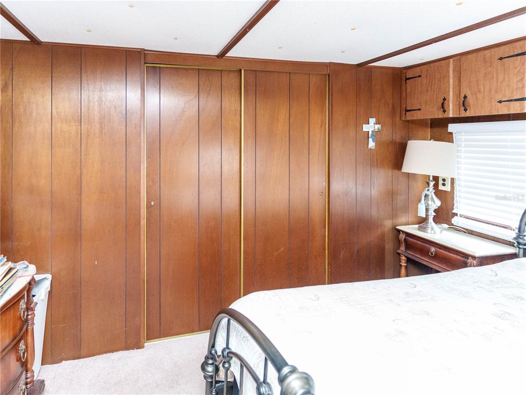 A bedroom features wood-paneled walls, a sliding closet door, and a bed with a metal frame — 5539 OAK RIDGE AVENUE, NEW PORT RICHEY, FL