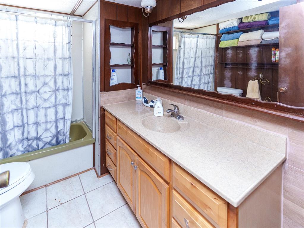 A bathroom features a wood vanity with a beige countertop, a tub-shower, and open shelving — 5539 OAK RIDGE AVENUE, NEW PORT RICHEY, FL