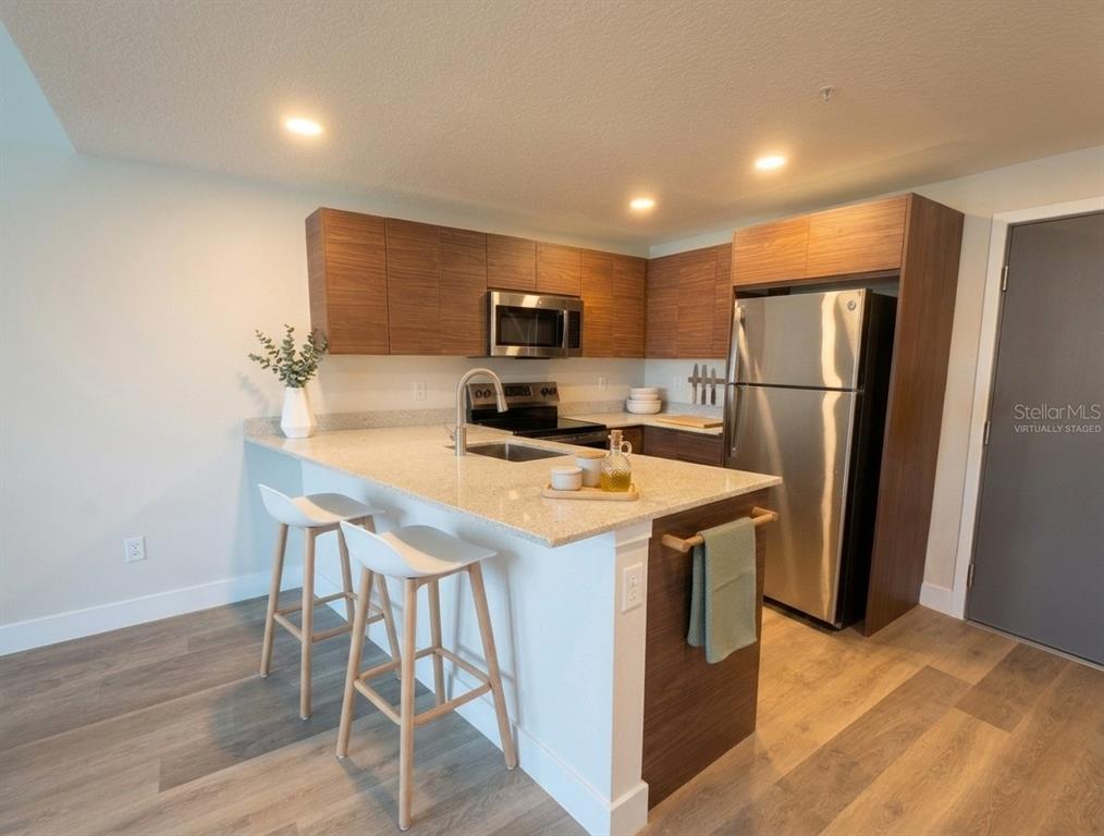 A modern kitchen features wood-grain cabinets, stainless steel appliances, and a granite-topped breakfast bar — 4424 S TEXAS AVENUE UNIT 104, ORLANDO, FL
