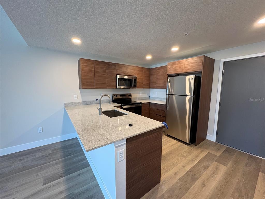 A modern kitchen features wood-grain cabinets, granite countertops, and stainless steel appliances — 4424 S TEXAS AVENUE UNIT 104, ORLANDO, FL