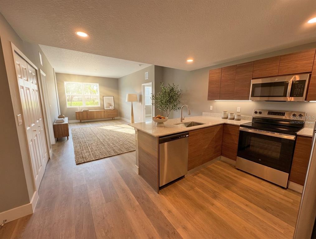 A kitchen with wood-toned cabinets and stainless steel appliances opens into a living area — 4424 S TEXAS AVENUE UNIT 104, ORLANDO, FL