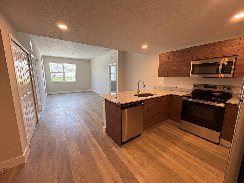 A kitchen with wood-tone cabinets and stainless steel appliances opens into a living area — 4424 S TEXAS AVENUE UNIT 104, ORLANDO, FL