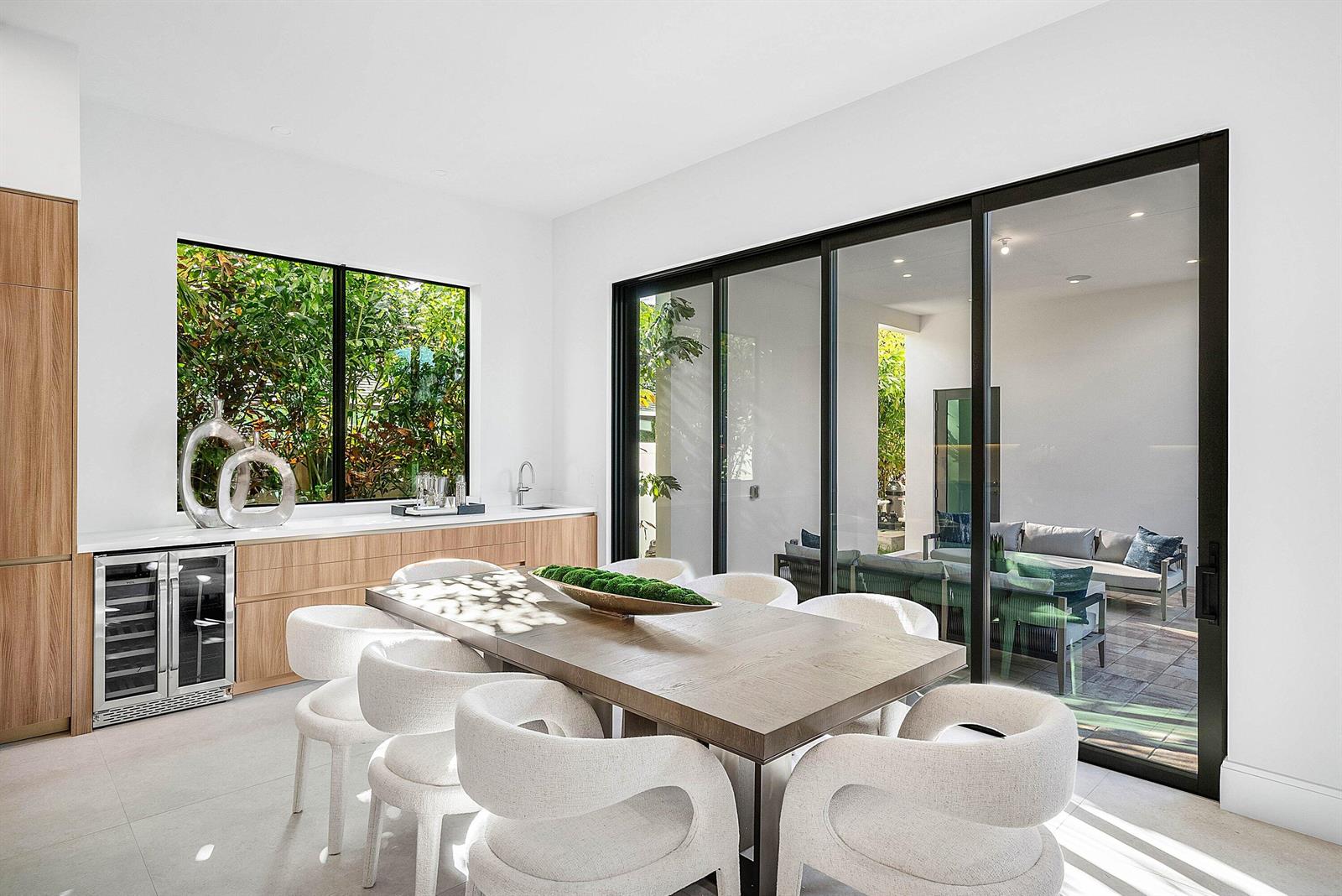 A modern kitchen and dining area features white cabinetry, wood accents, and a marble island — 222 SE 5th Street, Delray Beach FL 33483, DELRAY BEACH, FL