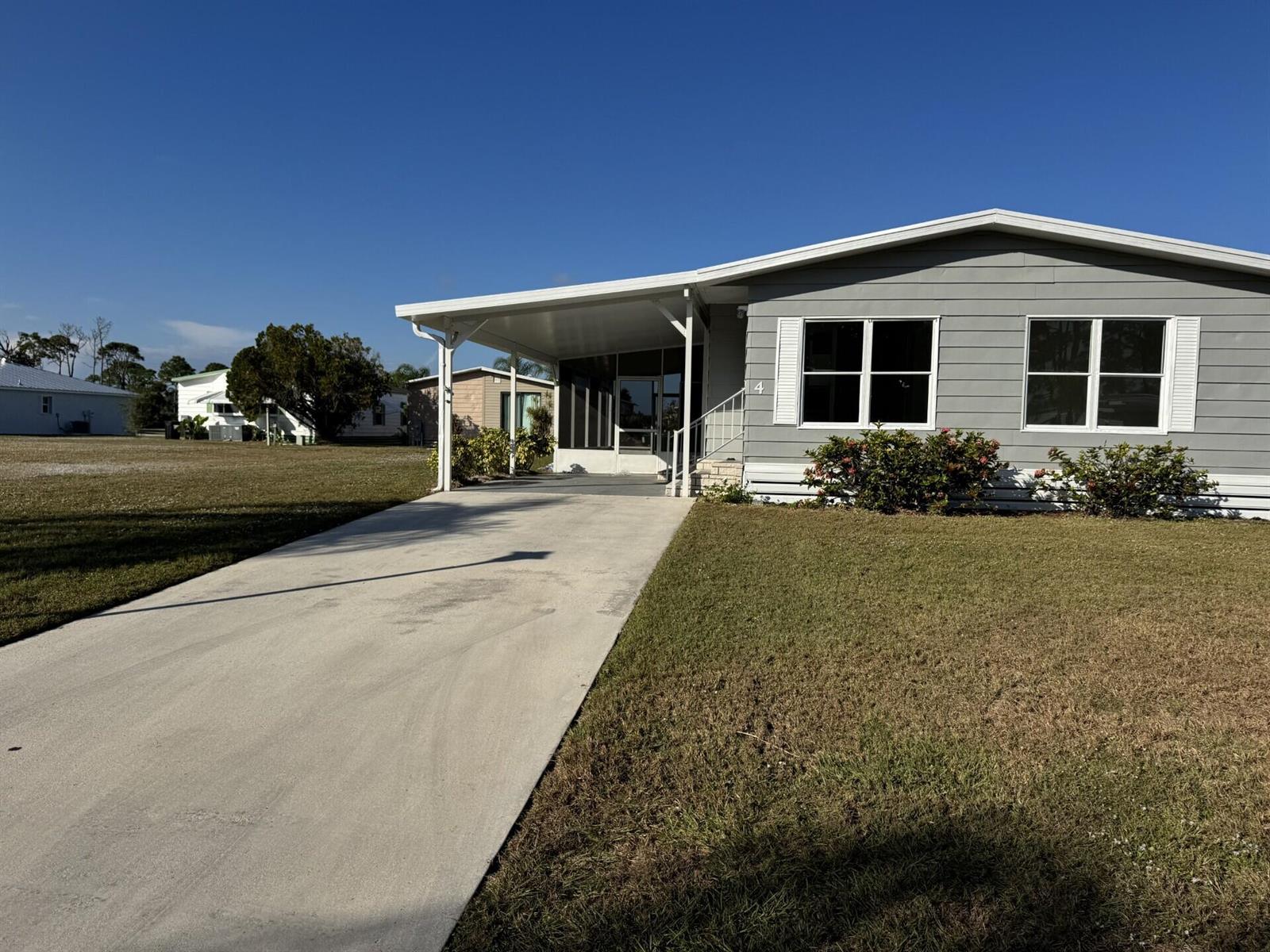 A gray manufactured home features a concrete driveway, a carport, and a screened-in front porch — 4 San Felipe, Fort Pierce FL 34951, FORT PIERCE, FL