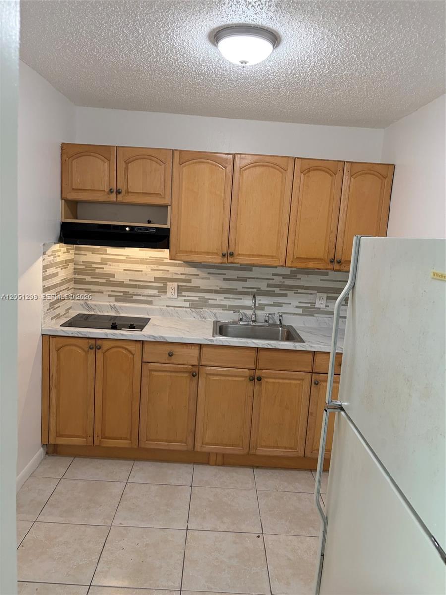 A small kitchen features light wood cabinets, a marble-look countertop, and a tiled backsplash — 6980 NW 186th St # 525A, Hialeah FL 33015, HIALEAH, FL