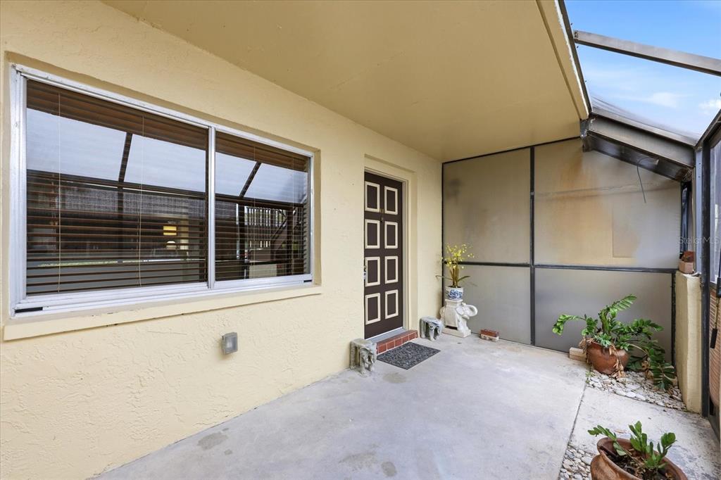 A covered patio features a concrete floor, a sliding window, and a dark brown door — 2420 WINDING CREEK BOULEVARD UNIT 105, CLEARWATER, FL