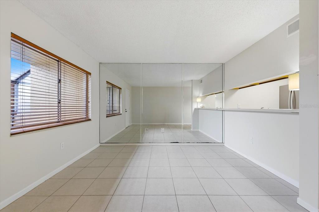A room with light-colored tile flooring, a large mirrored wall, and a window with blinds — 2420 WINDING CREEK BOULEVARD UNIT 105, CLEARWATER, FL