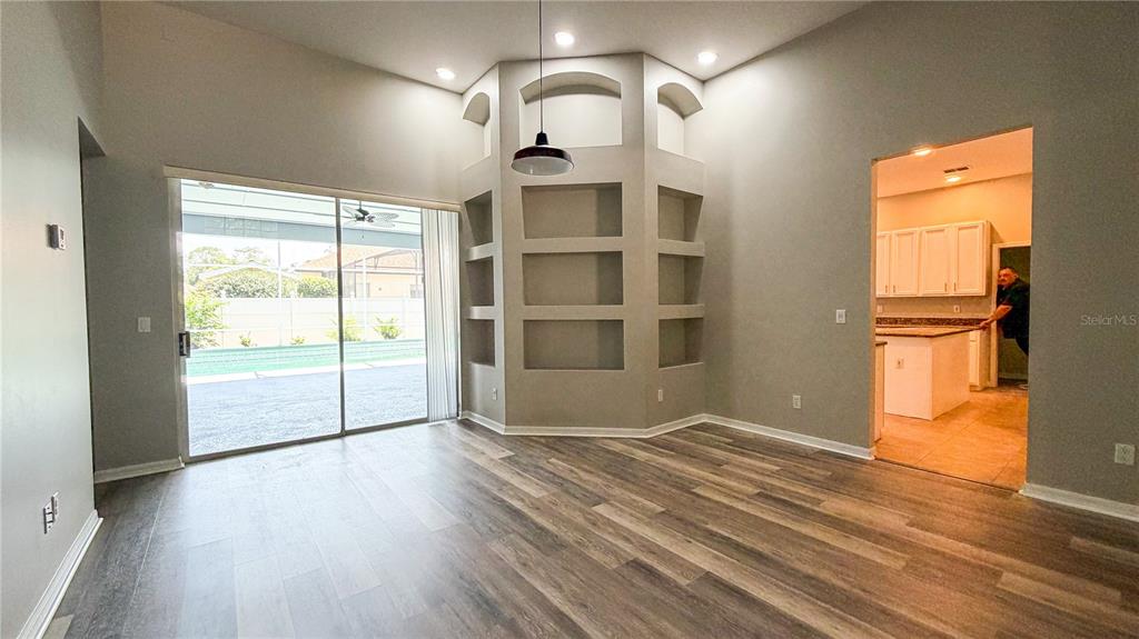 An open-concept living area features wood-look flooring, built-in wall niches, and a view into the kitchen — 123 GOLF COURSE PARKWAY, DAVENPORT, FL