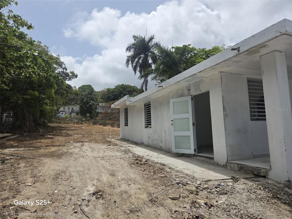 A white, single-story building sits on a dirt lot with trees and a palm tree — 144 CARRETERA 3, CEIBA, PR