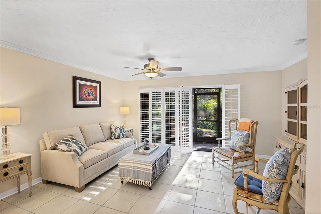 A living room features a beige sofa, two wooden chairs, tile flooring, and plantation shutters — 800 HUDSON AVENUE UNIT 106, SARASOTA, FL
