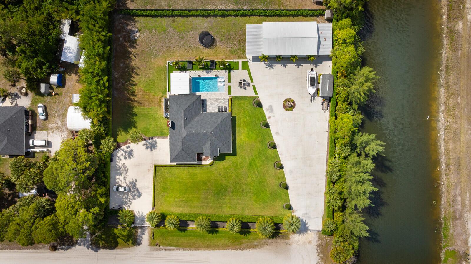 Aerial view of a house with a large lawn, detached garage, and a canal — 16966 91st Place N, FL 33470, FL