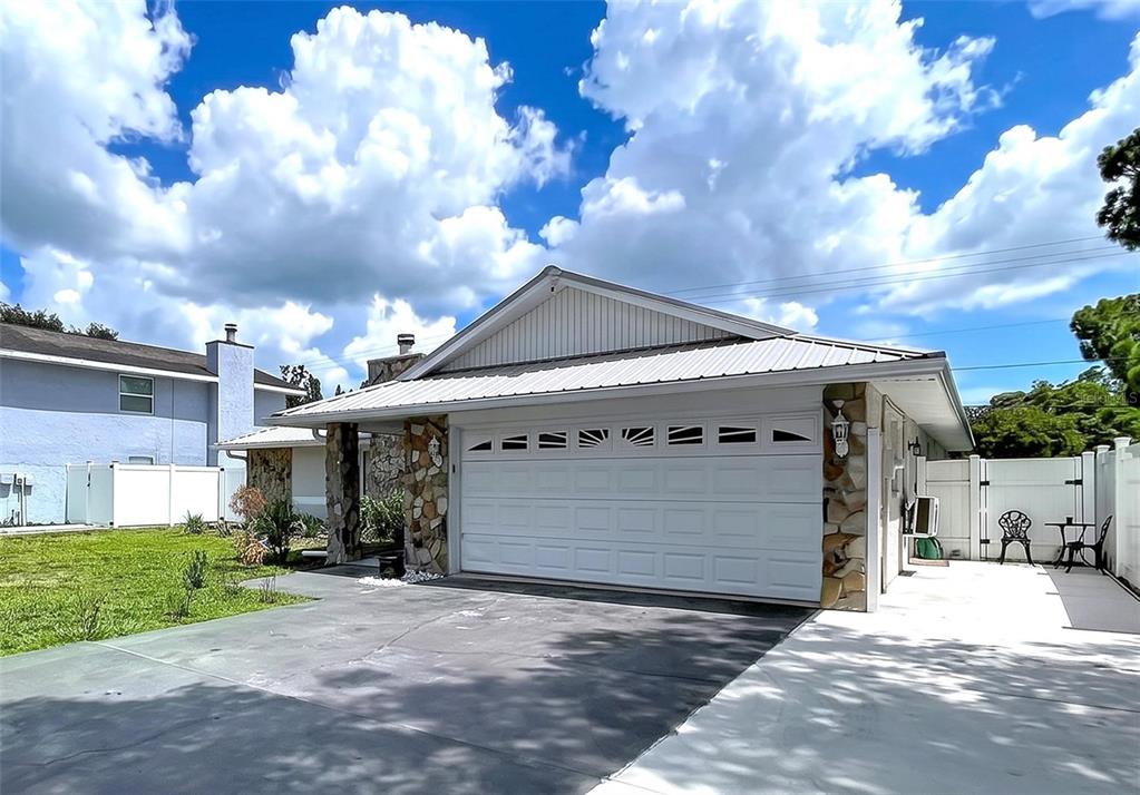 A single-story house exterior features a white garage door, stone accents, and a metal roof — 5520 FULMAR DRIVE, TAMPA, FL