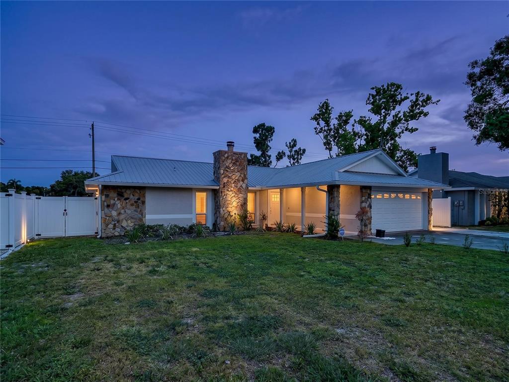 A single-story house with a stone chimney, metal roof, and attached garage at dusk — 5520 FULMAR DRIVE, TAMPA, FL