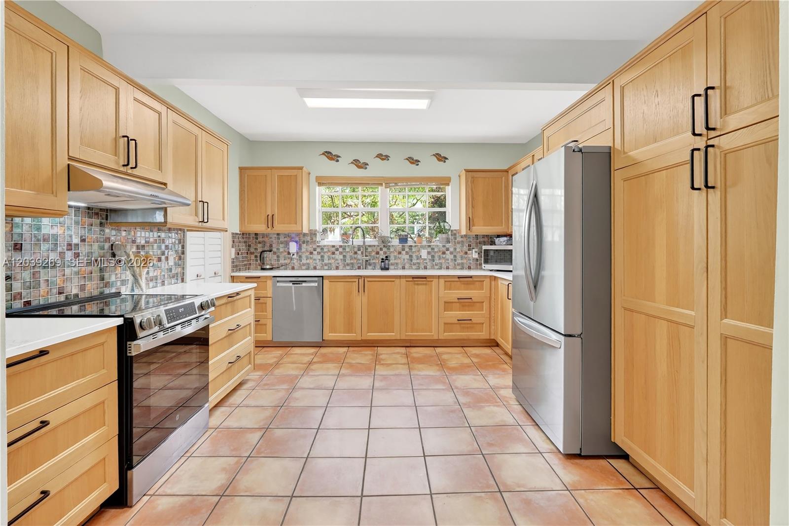 A kitchen features light wood cabinets, stainless steel appliances, a tiled backsplash, and terracotta flooring — 1642 SW 12th St, Miami FL 33135, MIAMI, FL
