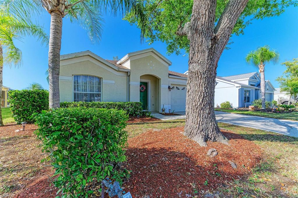 A single-story house with a beige exterior, a green front door, and a large tree — 4642 RUNABOUT WAY, BRADENTON, FL