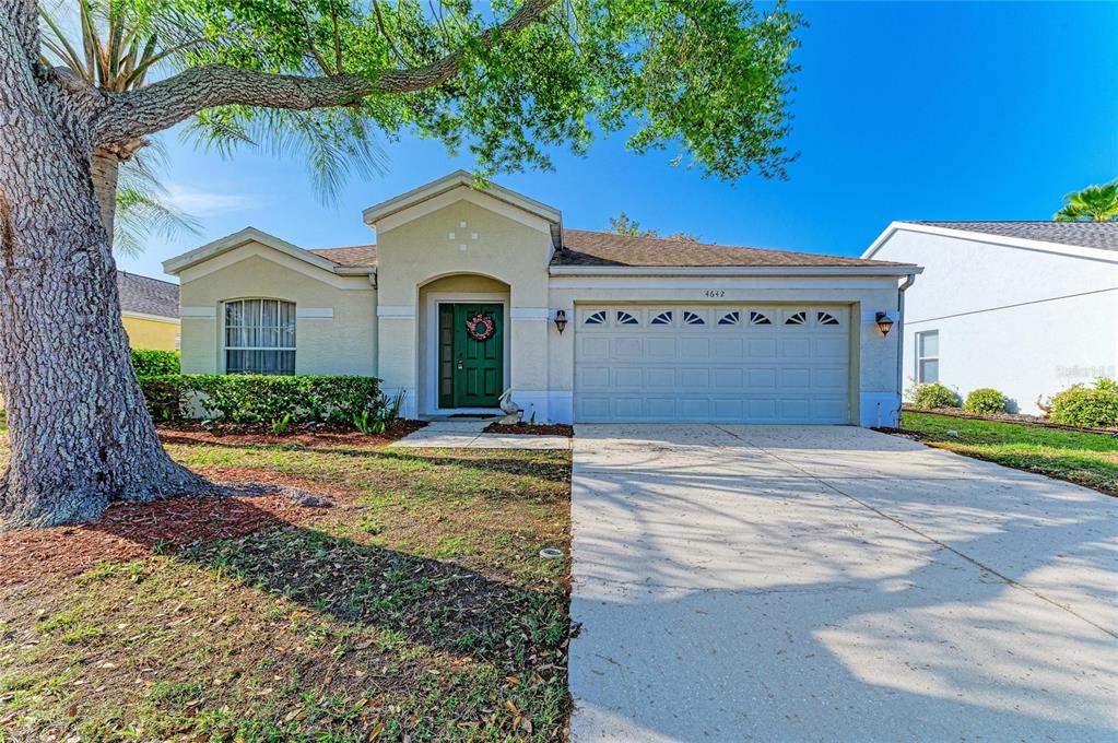 A single-story house with a beige stucco exterior, a two-car garage, and a large tree — 4642 RUNABOUT WAY, BRADENTON, FL