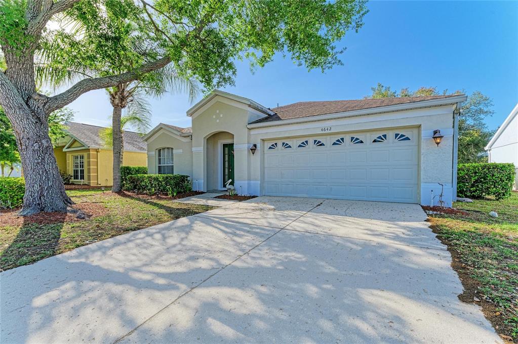 A single-story house with a beige stucco exterior, a two-car garage, and a large tree — 4642 RUNABOUT WAY, BRADENTON, FL