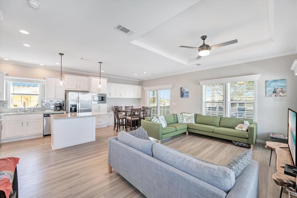 An open-concept kitchen and living area features light wood floors, white cabinetry, and green sofas — 20 BEAVERKILL DRIVE, LAKE WALES, FL