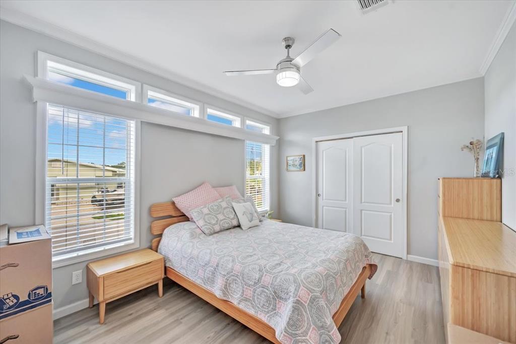 A bedroom features a bed, light wood furniture, a ceiling fan, and large windows — 20 BEAVERKILL DRIVE, LAKE WALES, FL