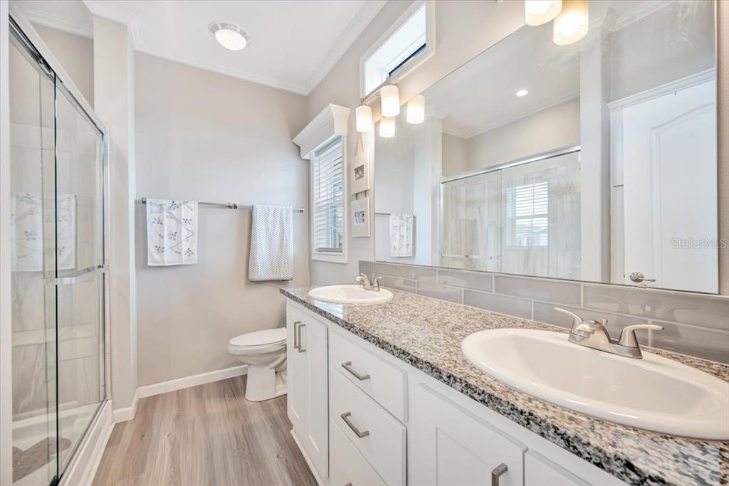 A bathroom features a double vanity with granite countertops, white cabinets, and a glass shower — 20 BEAVERKILL DRIVE, LAKE WALES, FL
