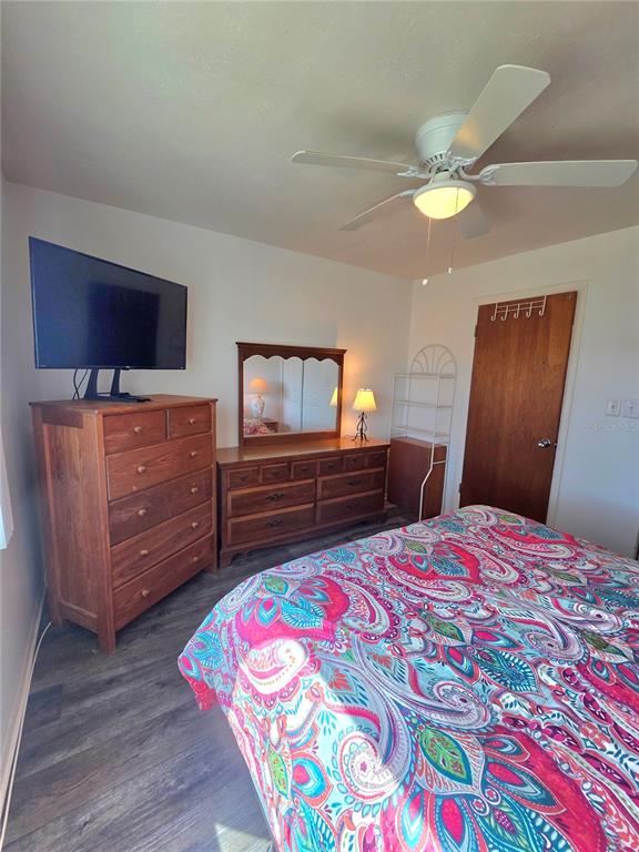 A bedroom features a wooden dresser with a television, a matching vanity, and a patterned bedspread — 1816 RESTFUL DRIVE UNIT M22, BRADENTON, FL