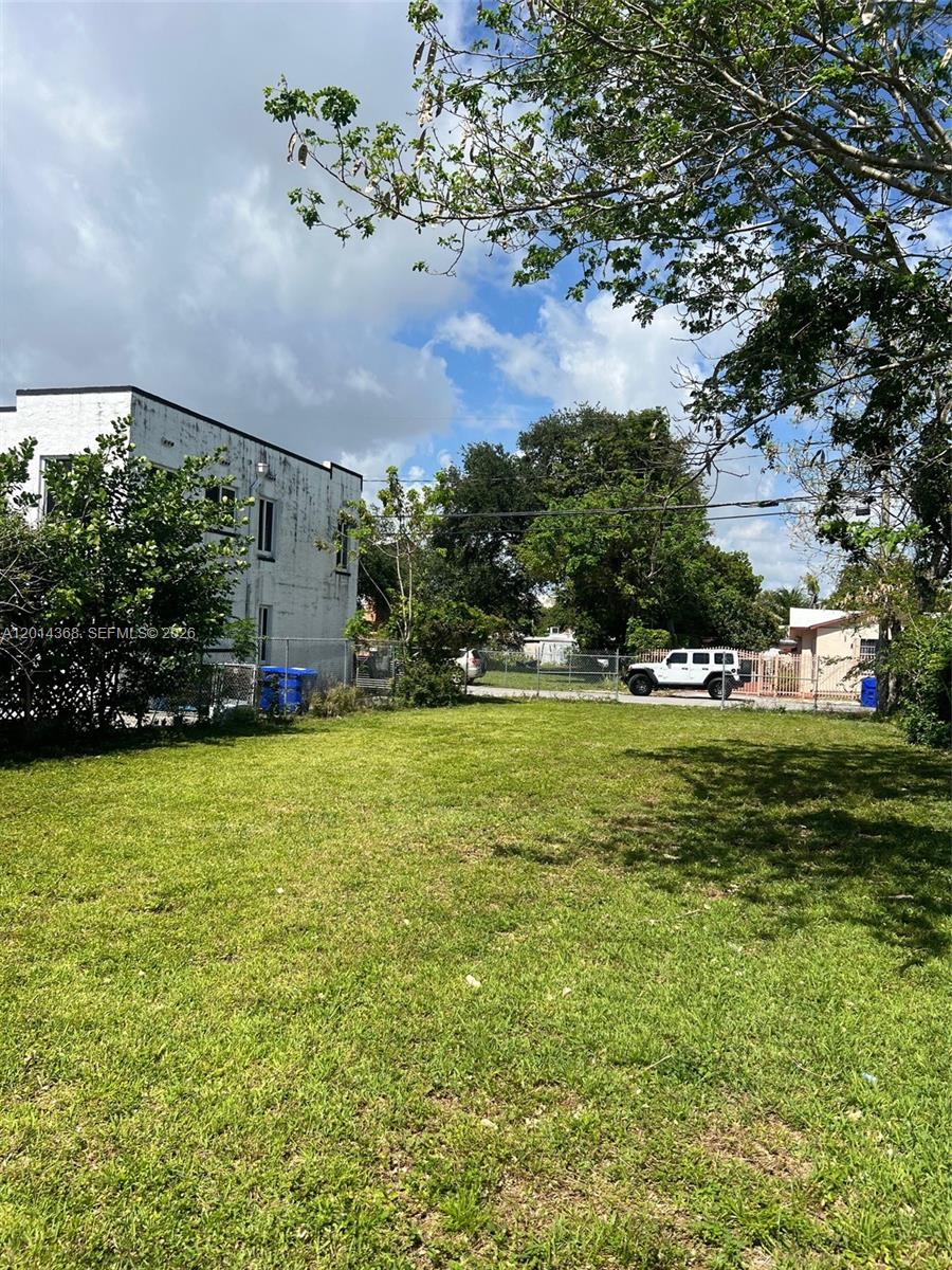 A grassy vacant lot sits next to a white building with a chain-link fence — 3033 NW 8th Ave, Miami FL 33127, MIAMI, FL