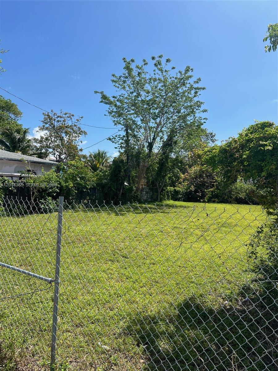 A chain-link fence encloses a grassy, vacant lot with trees under a clear blue sky — 3033 NW 8th Ave, Miami FL 33127, MIAMI, FL