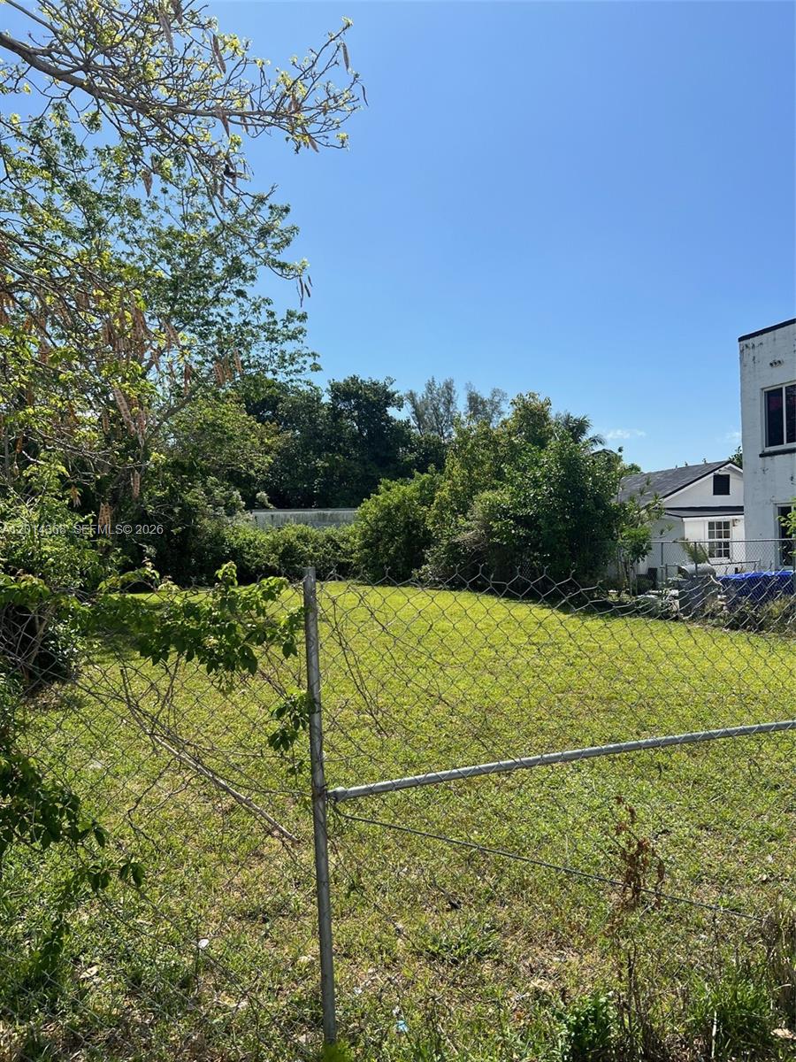 A fenced, grassy vacant lot is bordered by trees and adjacent residential buildings — 3033 NW 8th Ave, Miami FL 33127, MIAMI, FL