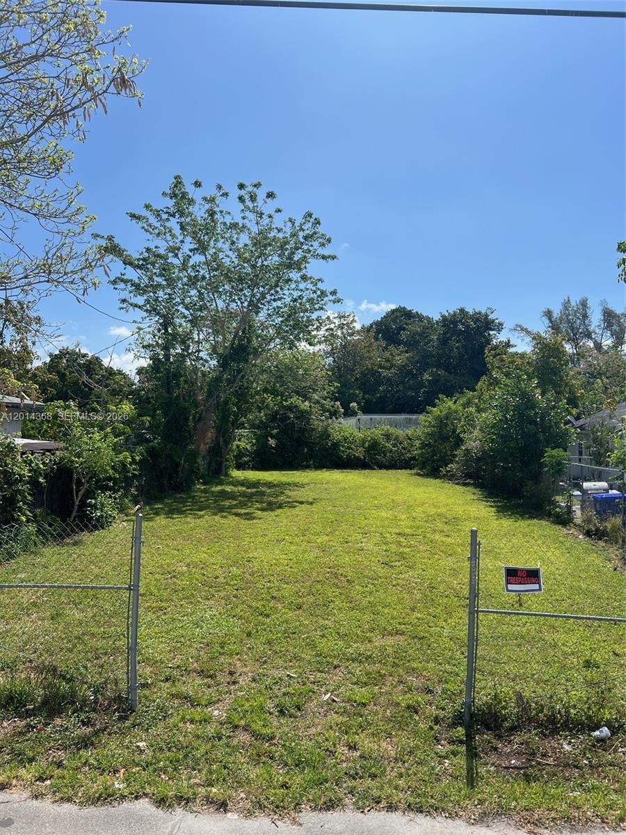 A fenced, grassy vacant lot is surrounded by trees and neighboring residential properties — 3033 NW 8th Ave, Miami FL 33127, MIAMI, FL