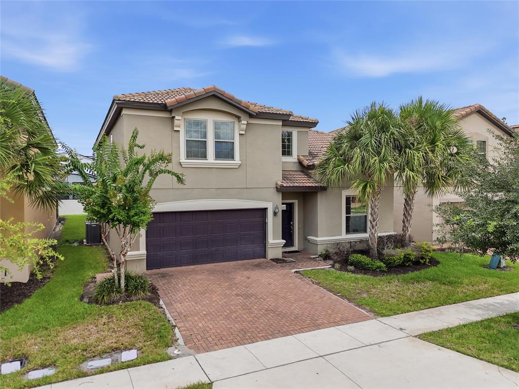 A two-story suburban house with a brick driveway, a dark garage door, and palm trees — 1610 LIMA AVENUE, KISSIMMEE, FL