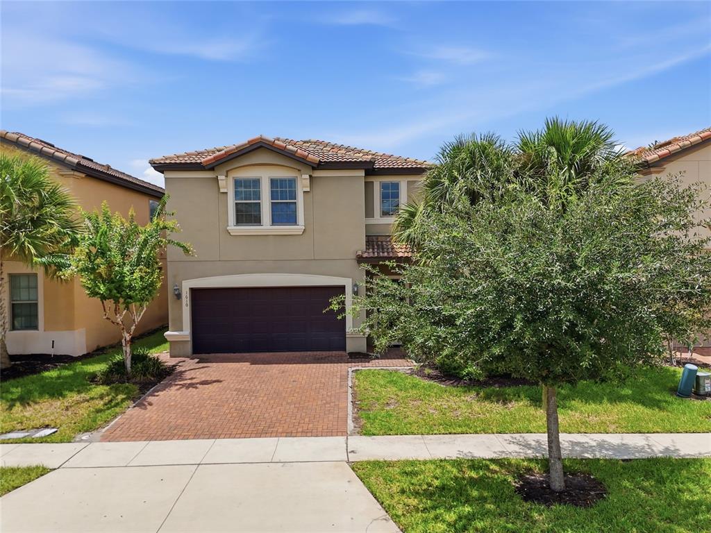 A two-story suburban house with a brown garage door, brick driveway, and front yard trees — 1610 LIMA AVENUE, KISSIMMEE, FL