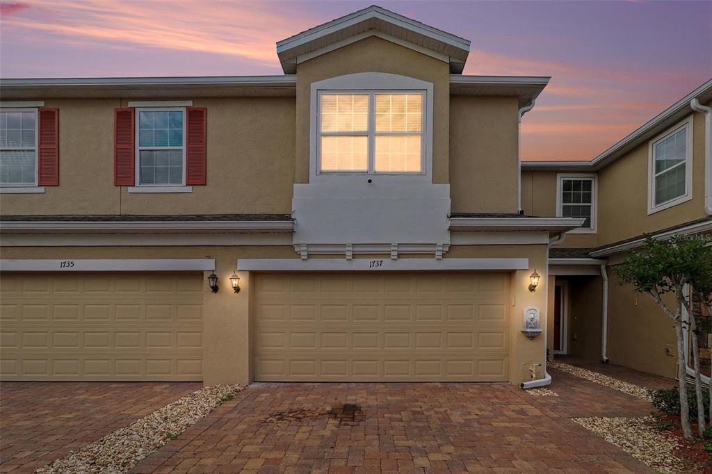 A two-story townhouse exterior features a tan stucco facade, a two-car garage, and red shutters — 1737 KATO WAY, KISSIMMEE, FL