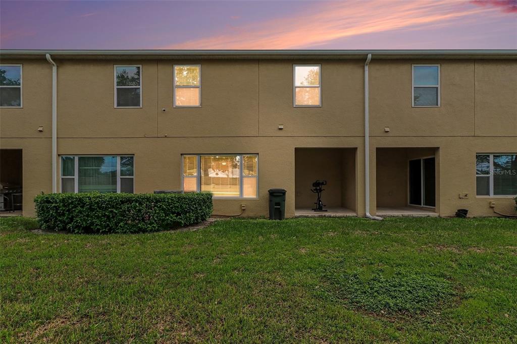 The rear exterior of a two-story tan townhouse features a grassy yard and patio area — 1737 KATO WAY, KISSIMMEE, FL