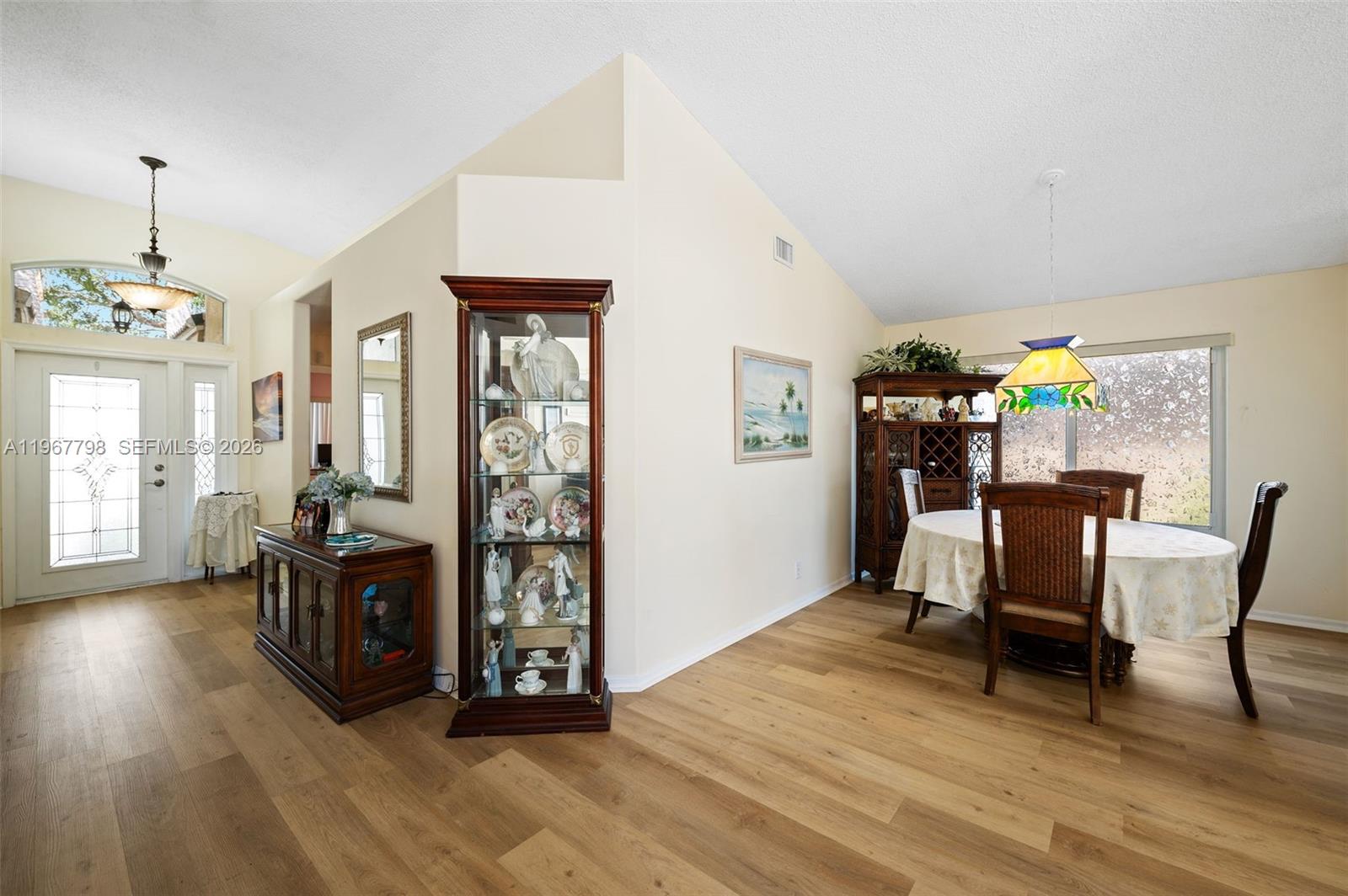 A dining area and entryway feature wood-look flooring, a glass display cabinet, and vaulted ceilings — 372 NW 45th Ter, Deerfield Beach FL 33442, DEERFIELD BEACH, FL