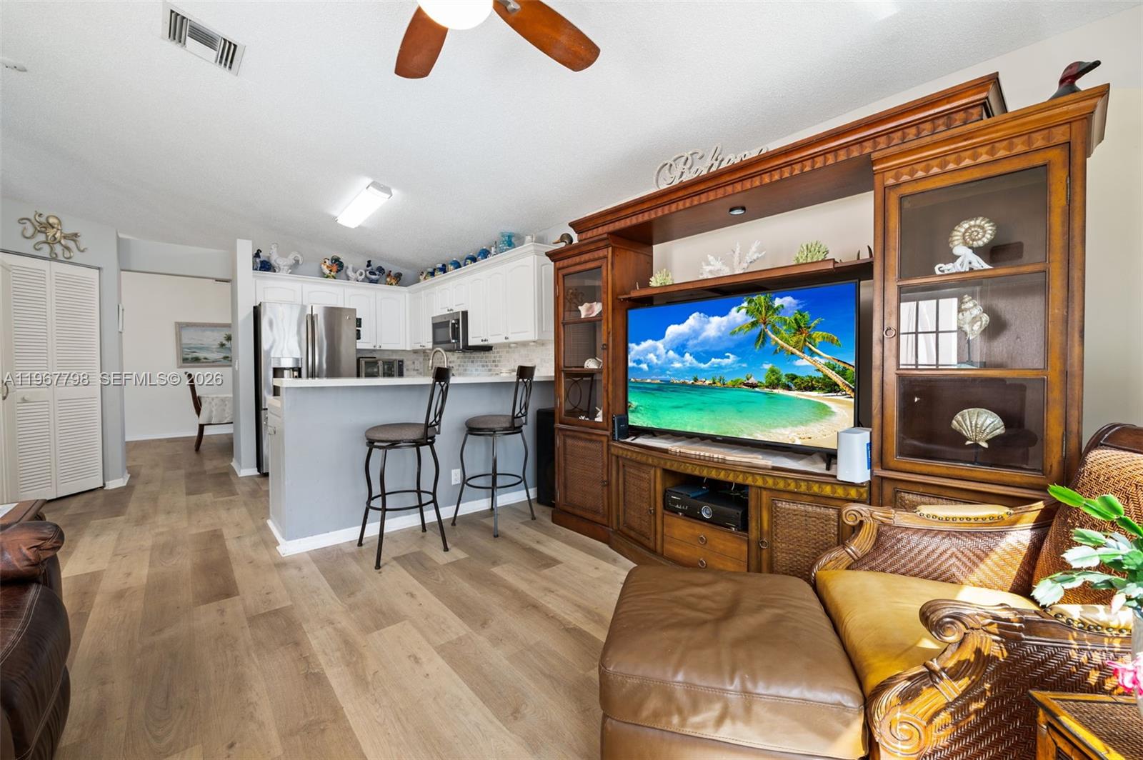 A living room with wood-look flooring features a large wooden entertainment center and kitchen bar — 372 NW 45th Ter, Deerfield Beach FL 33442, DEERFIELD BEACH, FL
