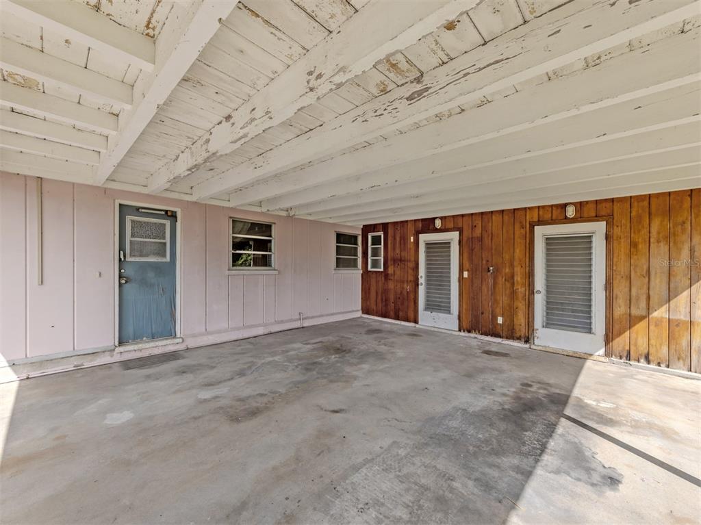 A concrete carport features a white wood-beam ceiling, pink siding, and wood-paneled walls — 730 S VENICE BOULEVARD, VENICE, FL