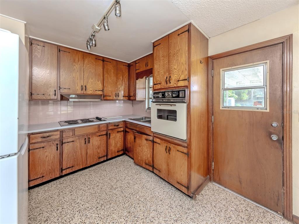 A kitchen features wood cabinets, a built-in wall oven, a cooktop, and speckled flooring — 730 S VENICE BOULEVARD, VENICE, FL